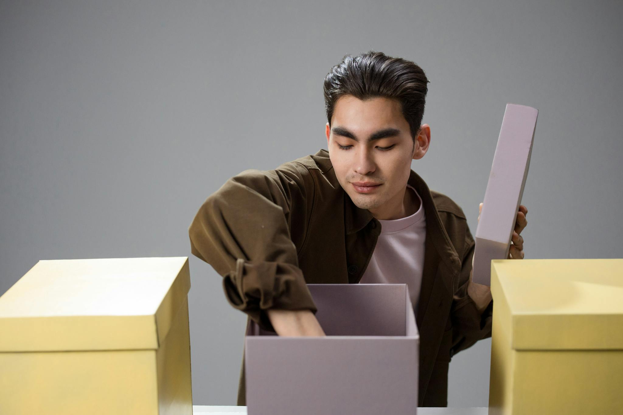 A young Asian man explores contents inside boxes, creating curiosity and engagement.